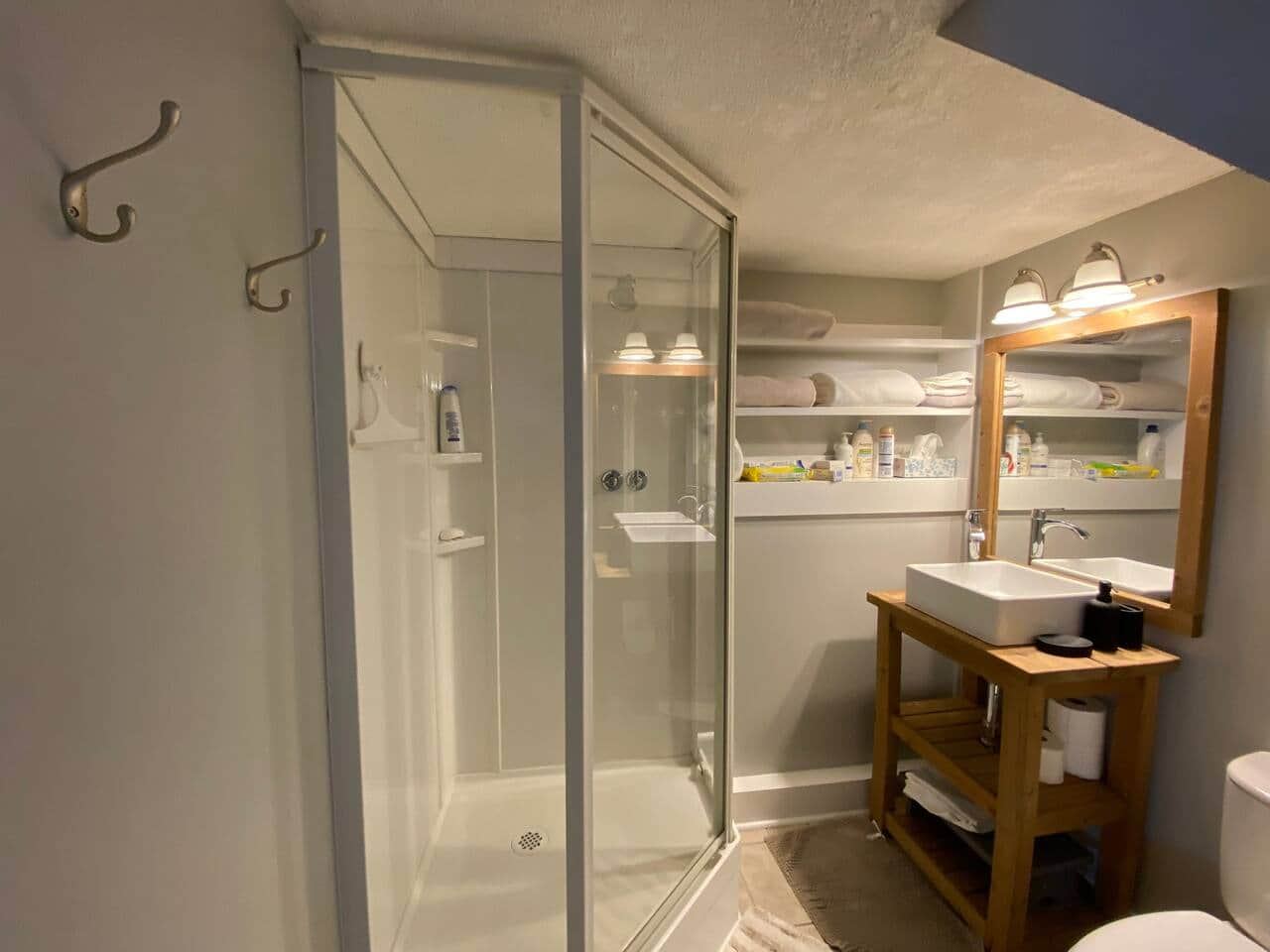 Bathroom glass shower beside a wooden vanity and vessel sink