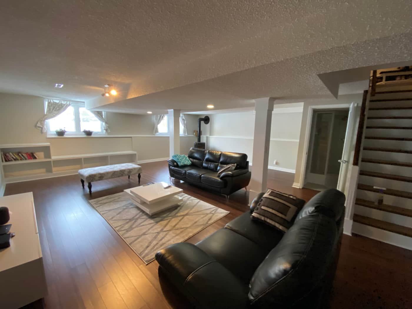 Spacious basement lounge with black leather sofas, a coffee table, and windows